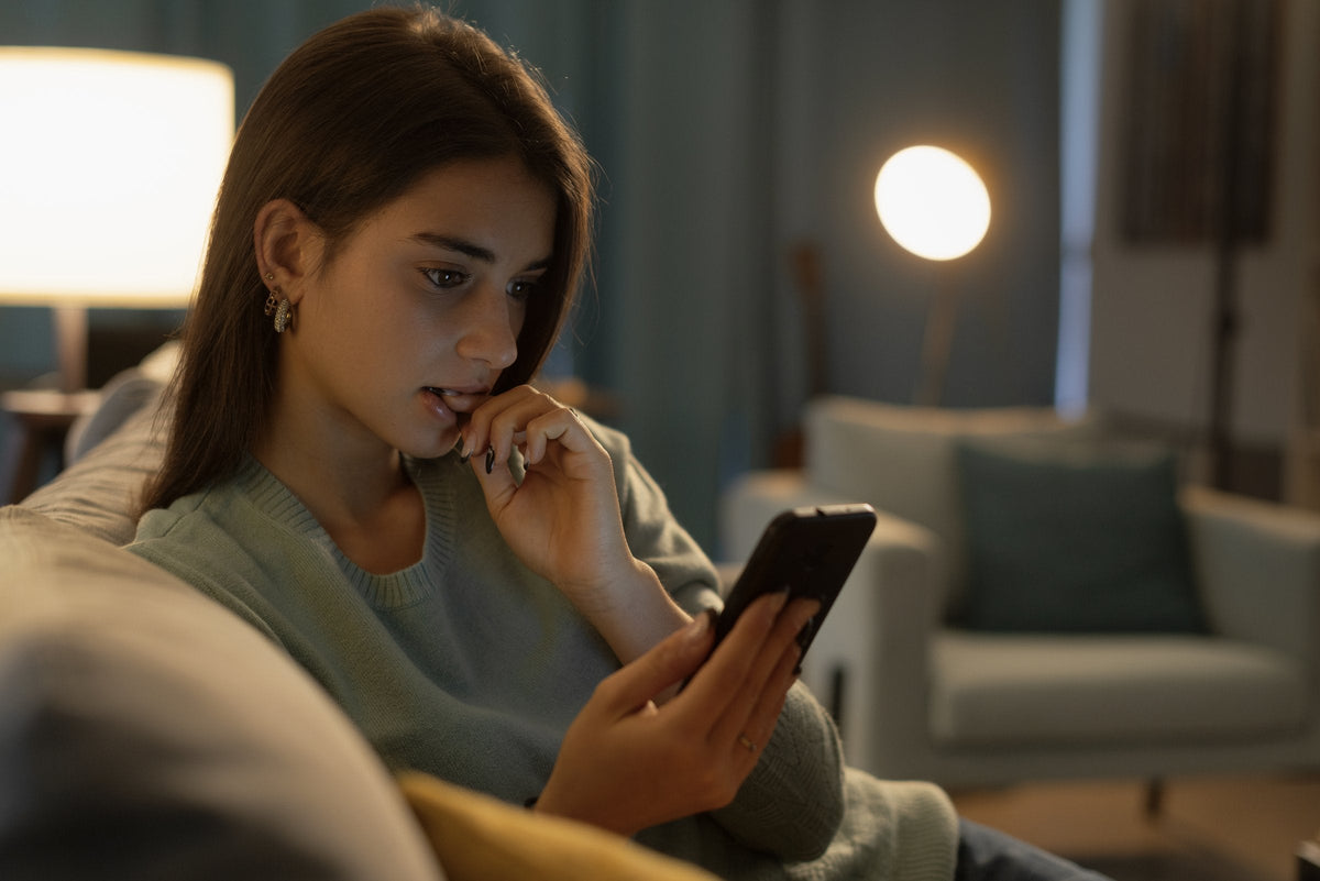 A young woman on her couch at night, thinking as she looks at her phone