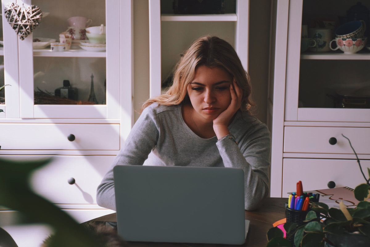A young woman at her table resting her head on her hand, staring at her laptop without starting
